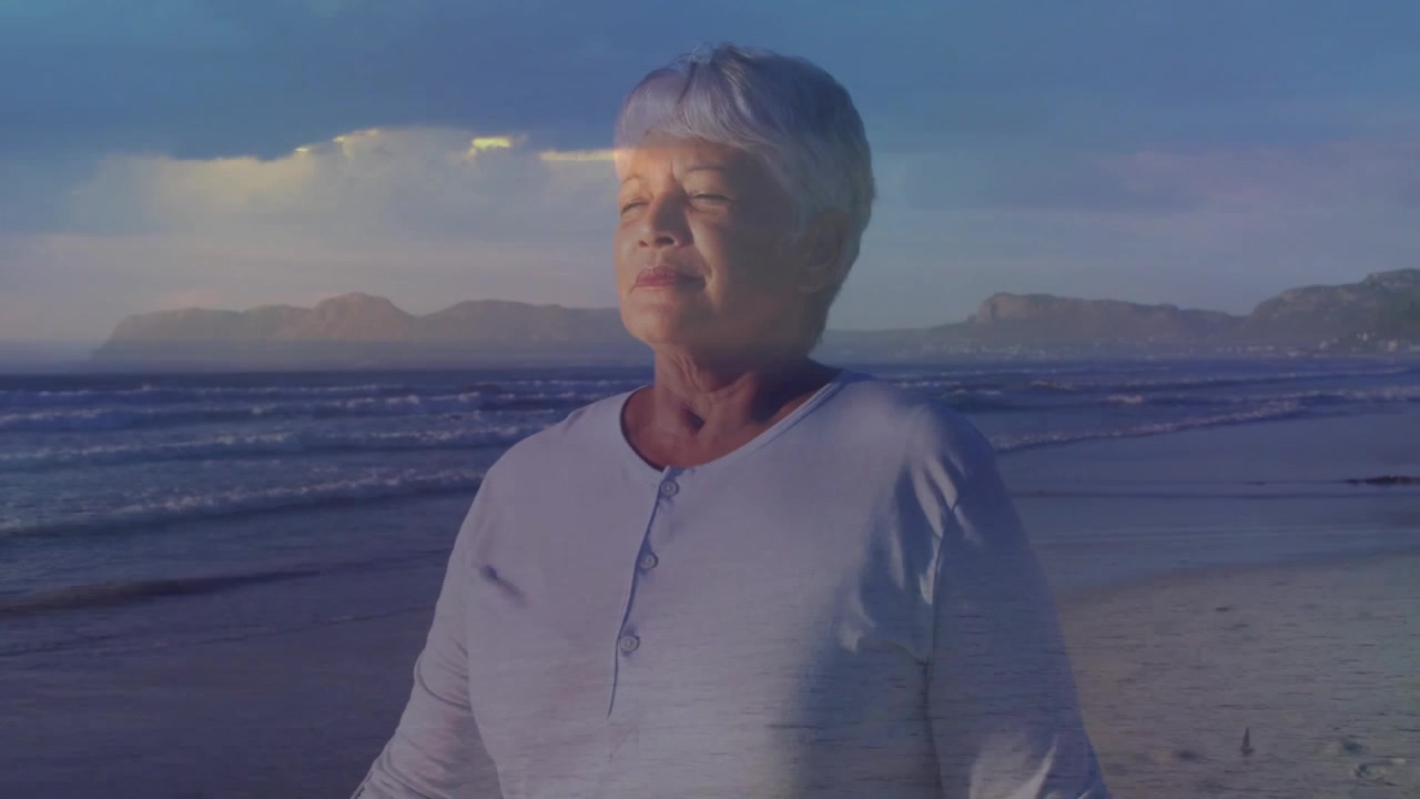 Senior woman standing at shore closing eyes and breathing as sun warming face for health