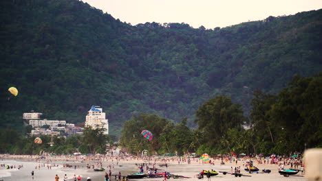 Weitwinkelaufnahme,-Die-Den-überfüllten-Strand-Von-Patong-In-Thailand-Mit-Grünen-Bergen-Im-Hintergrund-Zeigt-–-Menschen,-Die-Spaß-An-Wasseraktivitäten-Haben