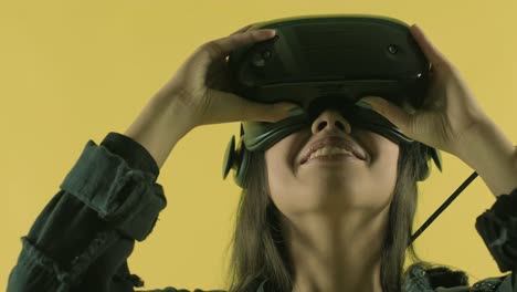 young woman puts on vr headset, looks around and wonders how amazing  in the vr world. virtual reality helmet on the yellow background