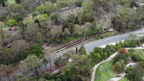 Drohne-Fliegt-über-Einen-Wunderschönen-Botanischen-Garten-Mit-Teich-Und-Fußweg-Zu-Einem-Friedhof-In-Der-Nähe