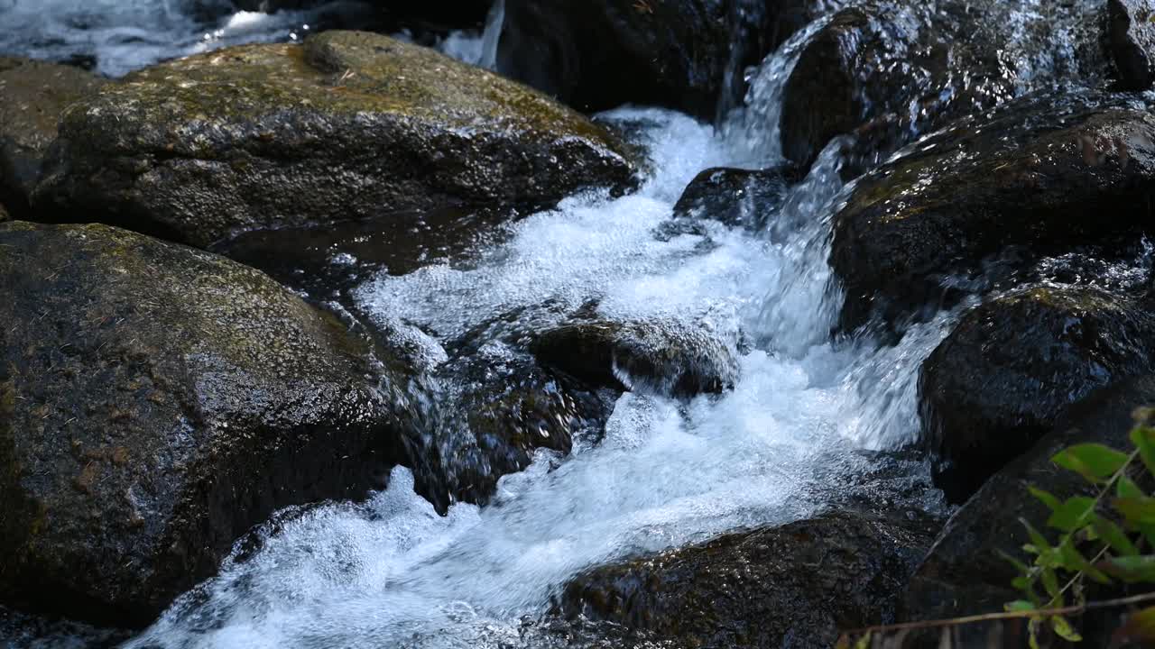 Ruscello di disgelo che scorre su rocce fluviali durante un'escursione, primo piano.