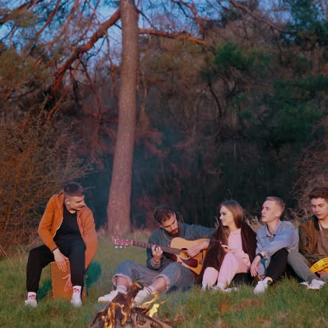 friends sitting around bonfire. cheerful friends singing songs and playing guitar near bonfire