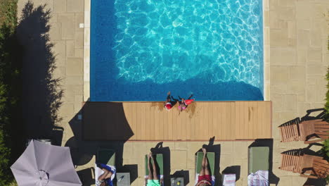 drone shot of multi-generation family on christmas holidays sitting by swimming pool in santa hats