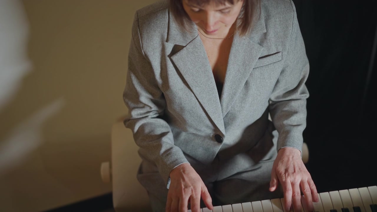 Mani di pianista donna bianca sulla tastiera, lezione intima in studio con insegnante in blazer che dimostra la tecnica, primo piano delle dita che articolano la melodia, illuminazione ambientale calda, espressione concentrata