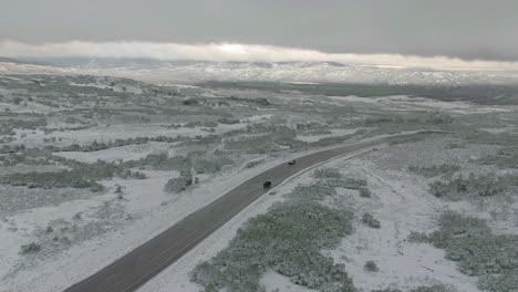 Aerial view pans up to show cars onf snowy mountain road