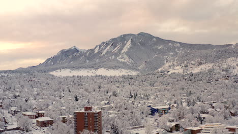 High-drone-shot-moving-forward-of-Boulder-Colorado-and-rocky-Flatiron-mountains-after-large-winter-snow-storm-covers-trees,-homes,-streets,-and-neighborhood-in-fresh-white-snow-for-the-holidays