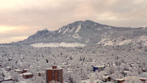 high drone shot moving forward of boulder colorado and rocky flatiron mountains after large winter snow storm covers trees, homes, streets, and neighborhood in fresh white snow for the holidays