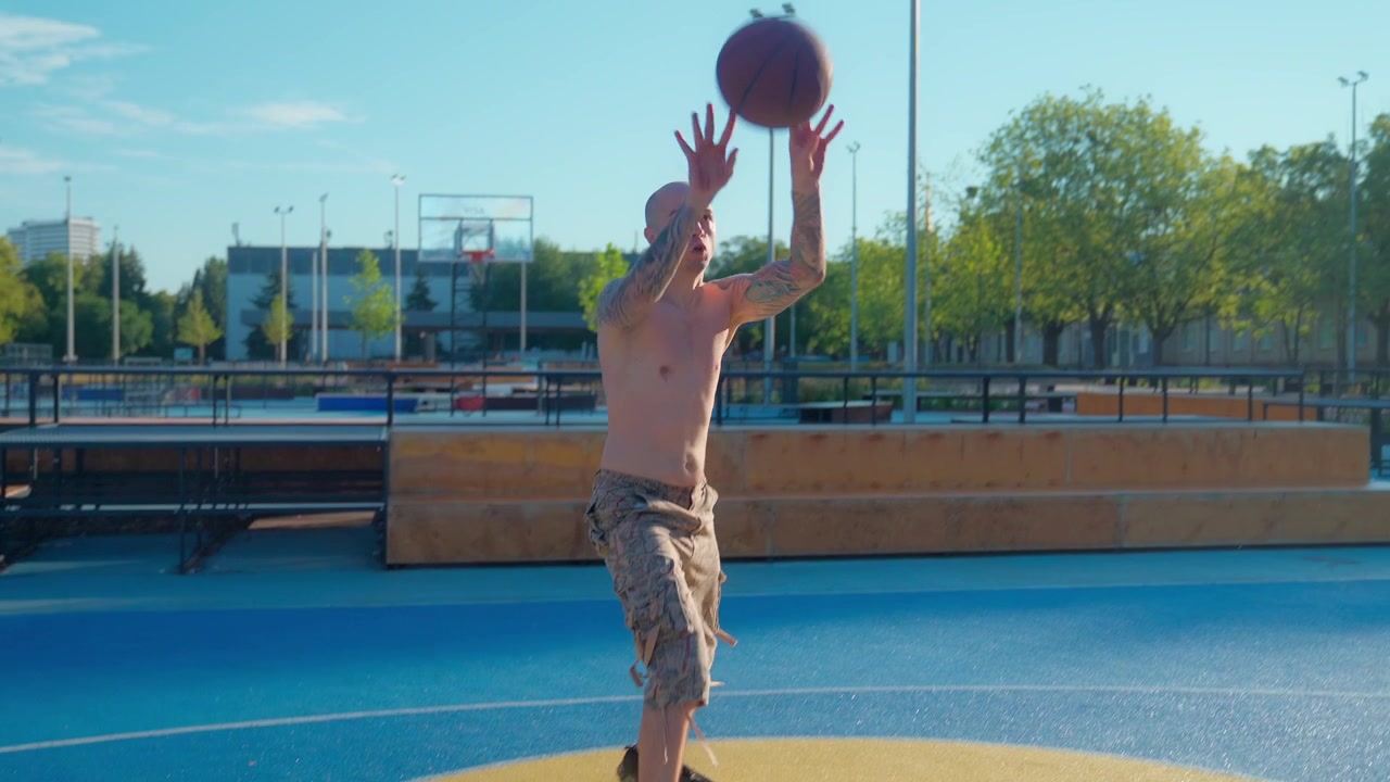 Uomo calvo tatuato che palleggia e tira a canestro su un campo da basket all'aperto
