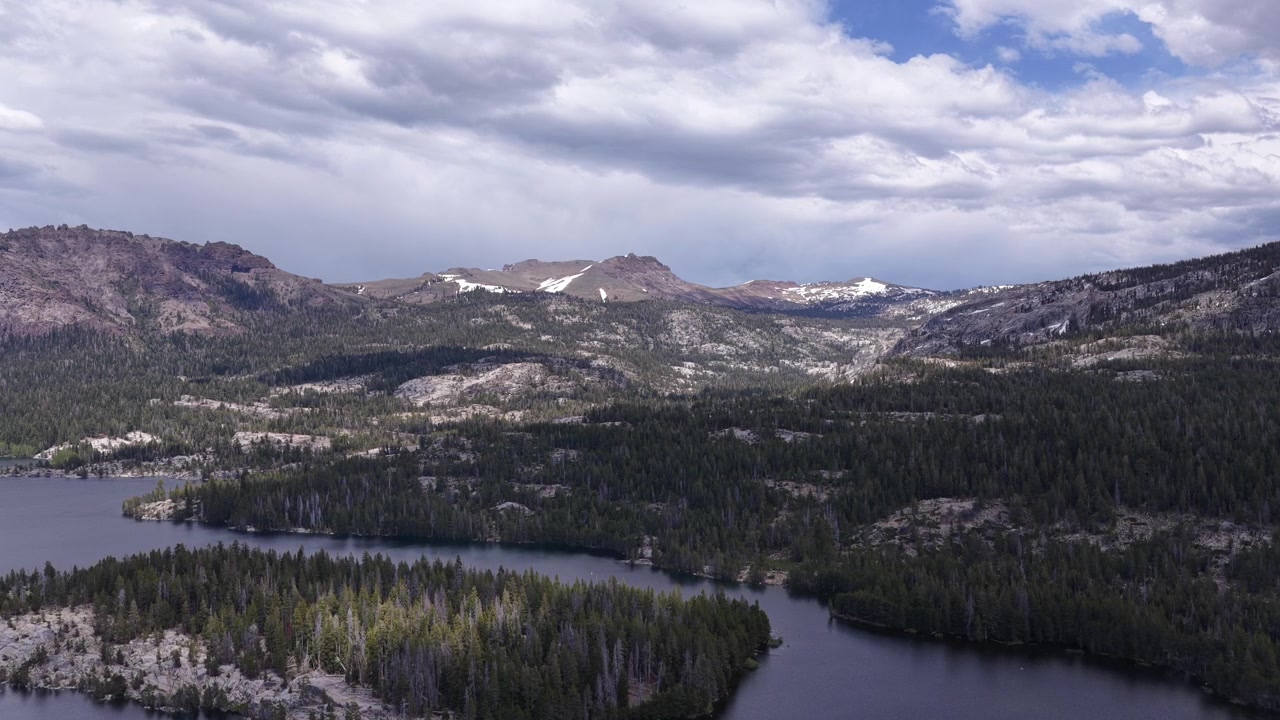 Splendida vista aerea del Lago Silver in California, che mostra una vasta pineta che circonda l'acqua, con montagne innevate in lontananza sotto un cielo nuvoloso e drammatico in una giornata di sole
