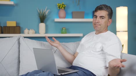 hombre usando una computadora portátil mirando impotente a la cámara.