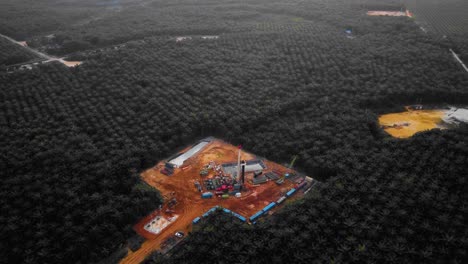 cinematic 4k drone footage of onshore drilling rig equipment structure for oil exploration and exploitation in the middle of jungle surrounded by palm oil trees during sunset and high oil price