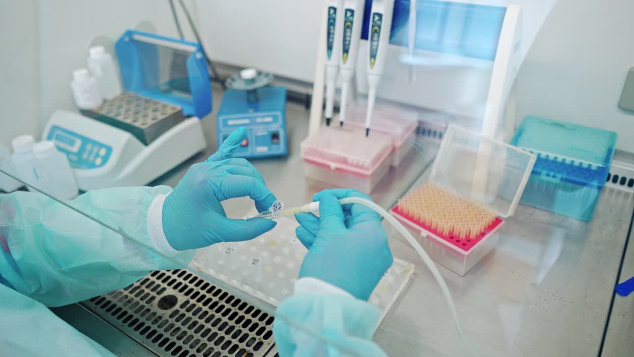 Hands in blue sterile gloves filling test tubes with liquid. Some racks with vials of liquid in modern laboratory indoors.