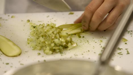 close-up of hands finely chopping pickles on a white cutting board