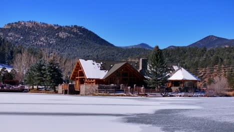 first snow ice frozen covered white evergreen lake house rocky mountain landscape scene front range denver aerial cinematic drone christmas ice skating hockey bluesky slow slide pan right motion