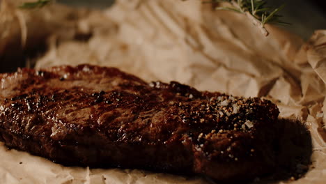 brown caramelized crust on juicy steak, paper surface, putting down twig of rosemary with kitchen tongs