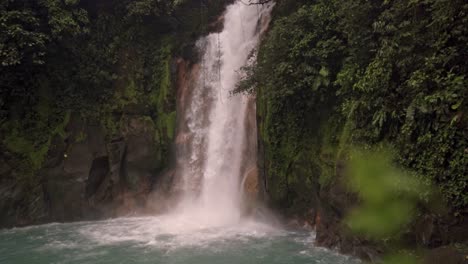 the dense, green rainforest foliage surrounds the scene, highlighting the mystical and ethereal atmosphere of the rio celeste waterfall in costa rica