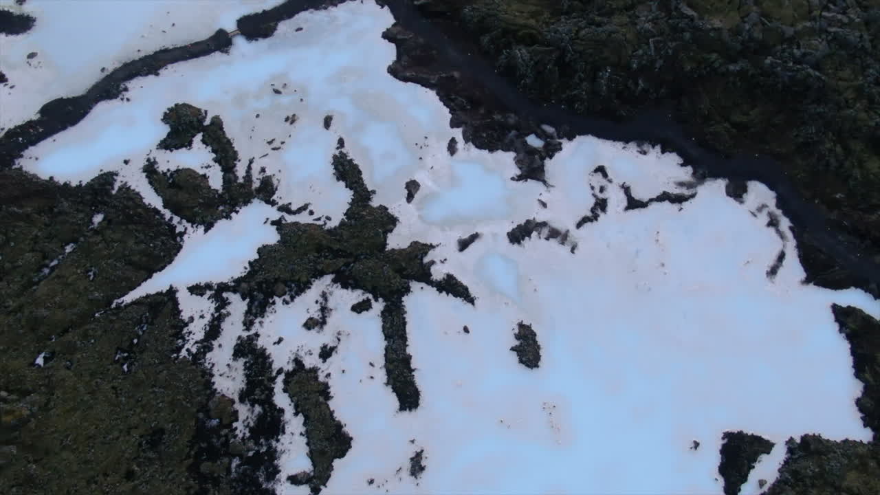 Breathtaking top down aerial spin view of a blue lagoon snow and ice covered rocky terrain in Iceland