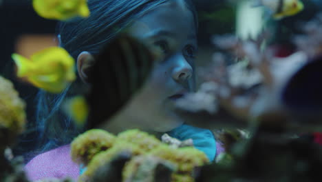 happy girl in aquarium looking at fish curious child watching colorful marine life swimming in tank learning about sea animals in underwater ecosystem inquisitive kid at oceanarium