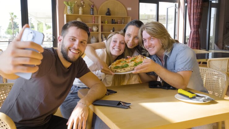 Gruppo di amici che si scattano un selfie e si divertono mentre mangiano la pizza in un ristorante 1