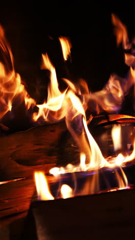 firewood burning slowly with sparks. wooden logs in flame inside the fireplace. detailed hot fire in the brickwork fireplace. cozy atmosphere. vertical video