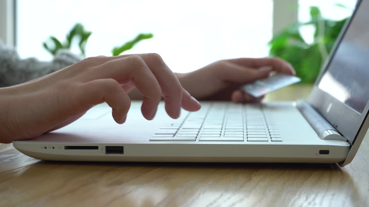 Girl holding a credit card layout and using her laptop while sitting in a cafe