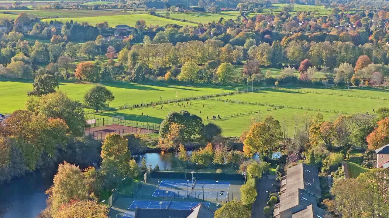 Panoramic drone flight over public parks, tennis courts, riverbank, gardens, autumn trees, residential area and rooftops in Wetherby, showing the vibrant landscape of West Yorkshire, England