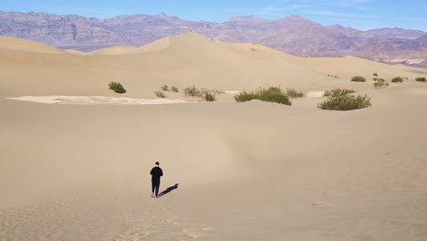 western caucasian male walking alone down a huge sand dune in the desert