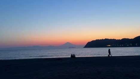 silhouette of people on a beach at sunset with distant mountain, tranquil and serene