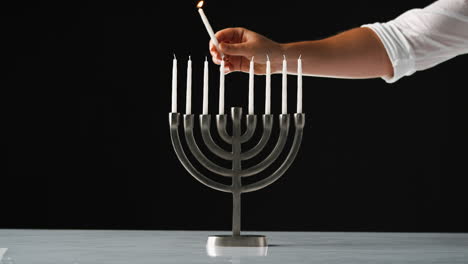 hand lighting the nine white candles in a jewish menorah sat on a pale marble surface, close up, front view