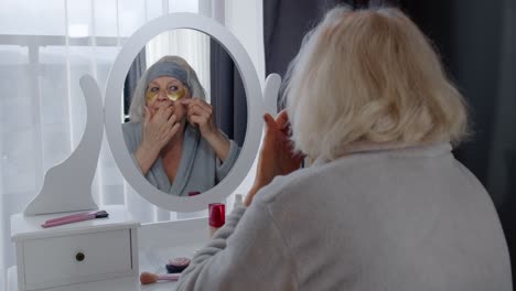 Old-senior-woman-grandmother-taking-care-of-skin-near-eyes-and-wrinkles,-putting-makeup-on-at-home