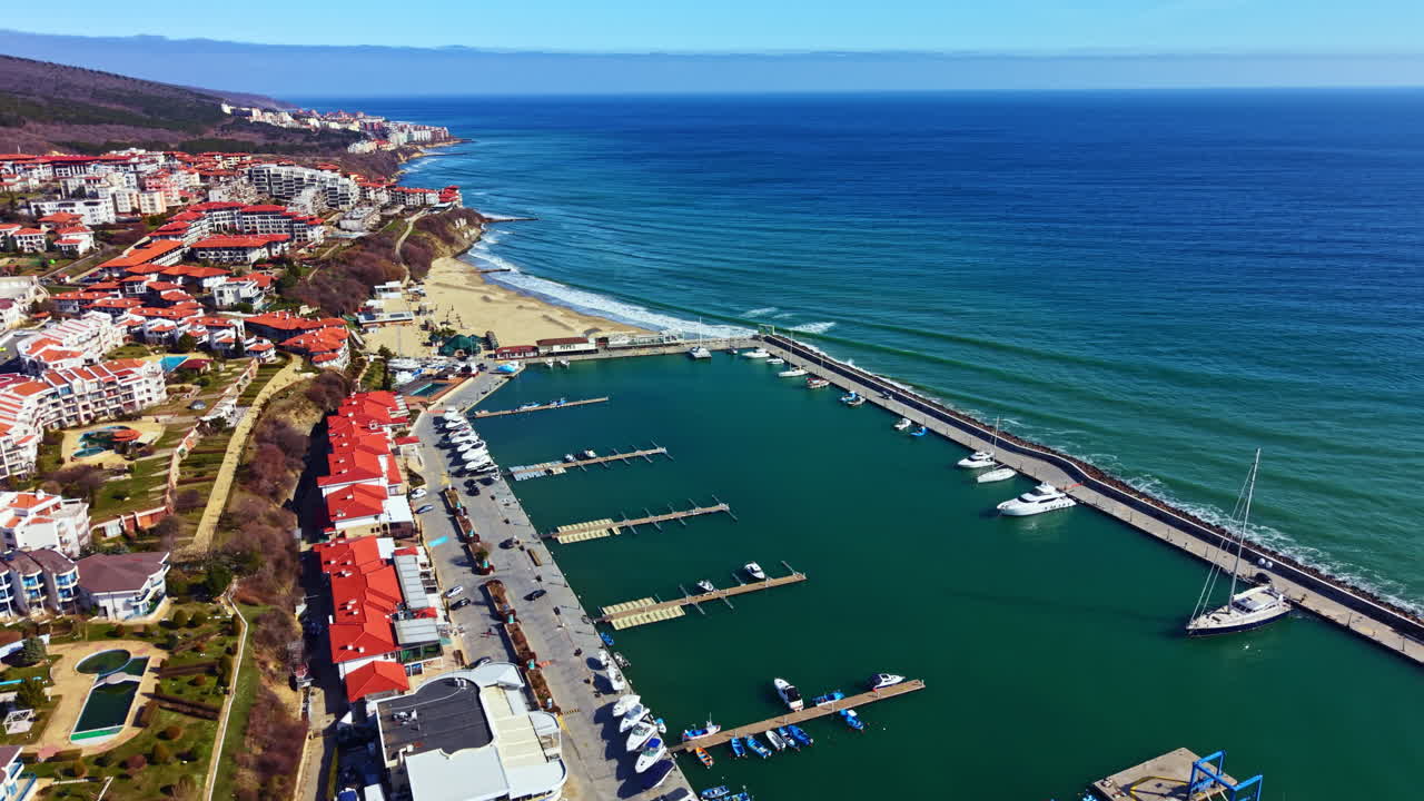 Scena costiera con barche ormeggiate al porto turistico ed edifici residenziali sulla riva durante una giornata limpida sul lungomare