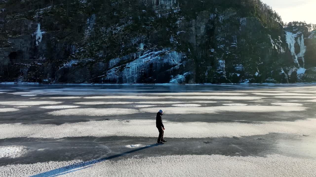 Un pattinatore sul ghiaccio scivola su un fiordo norvegese ghiacciato mentre un drone si muove da dietro a davanti in un suggestivo paesaggio invernale