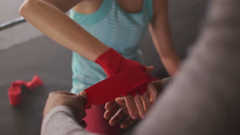 Video-of-hands-of-diverse-woman-and-man-tying-tapes,-preparing-for-box-training-at-gym