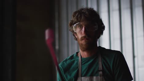 caucasian male blacksmith holding hot metal tool in workshop