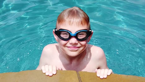 kaukasischer junge im alter von 10 jahren, der in zeitlupe mit brille und lächeln aus dem wasser in einem pool kommt