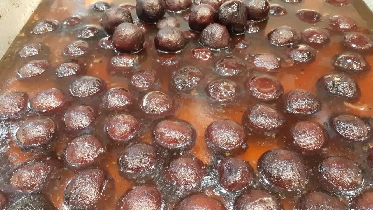 Indian Traditional Juicy Gulab Jamun in Large Steel Pan available for sale in the market. The Indian sweet Gulab jamun. Gulab jamuns indian desserts. Pan Full of Syrup Laden Gulab Jamuns.