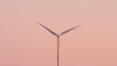wind turbine blades spin against a pastel pink sky at dusk in clean energy landscape, backdrop background