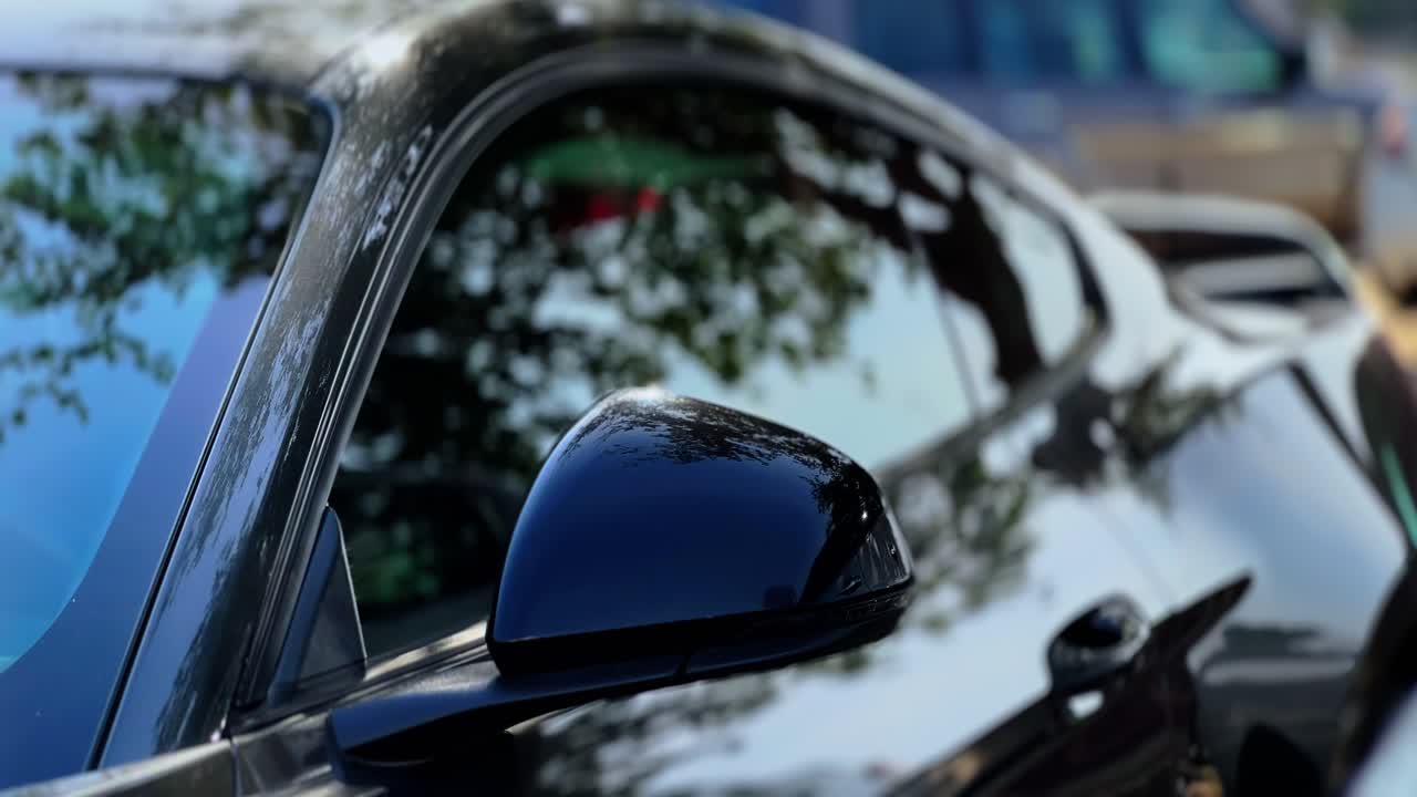 Cinematic 4K close-up of a luxury black car with tree reflections on the side mirror and window. Perfect for commercials, automotive ads, or high-end lifestyle visuals.