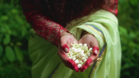 hands gently hold white arabian jasmine blooms against blurred green foliage backdrop