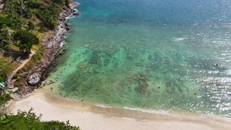 Drone footage captures a serene beach in Phuket, Thailand, showcasing turquoise waters, lush greenery, and a tranquil atmosphere