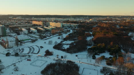 Aerial-birds-eye-shot-of-colorful-trees-with-snowy-winter-fields-and-residential-blocks-in-przymorze-district-of-Gdansk-at-sunrise