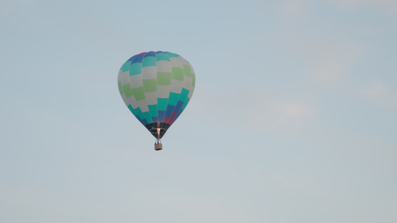 A vibrant hot air balloon lifts off into the sky as its burner fires, creating a warm glow against the morning light at the Canberra Balloon Spectacular.