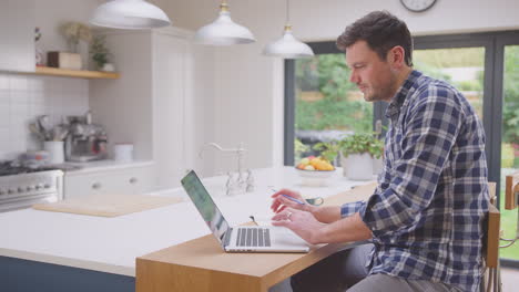 Hombre-Trabajando-Desde-Casa-Usando-Una-Computadora-Portátil-En-El-Mostrador-De-La-Cocina---Filmado-En-Cámara-Lenta