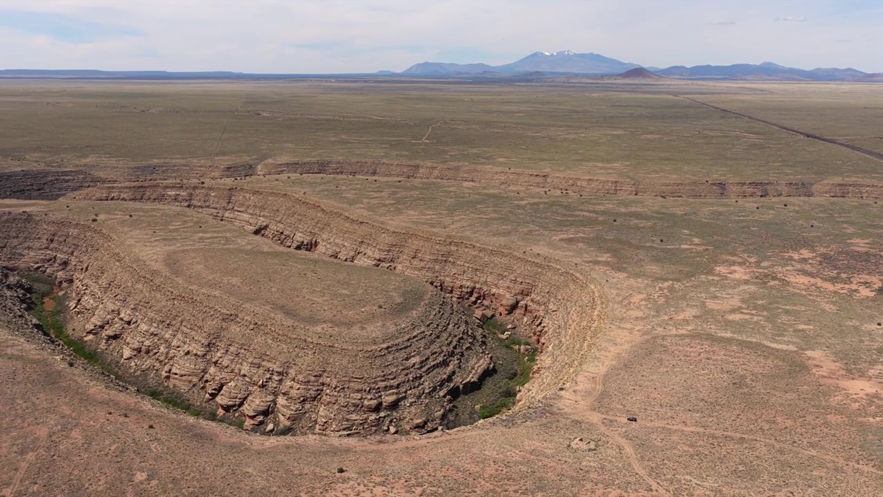 Vuelo de dron 4K UHD revelando un lecho de río seco profundo y en forma de herradura en el escarpado terreno de Arizona. Un coche negro aparcado cerca de los acantilados enfatiza el inmenso tamaño de este salvaje paisaje desértico
