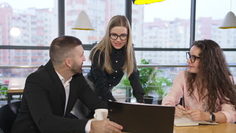 man in suit sits in front of his colleagues showing them papers in black folder. female employees look at the document, discussing it.