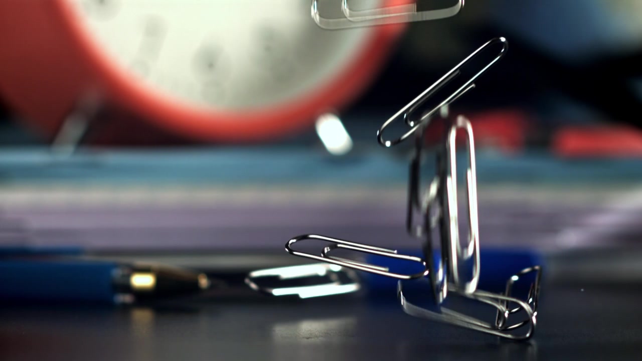 Paper clips falling onto an office desk in slow motion