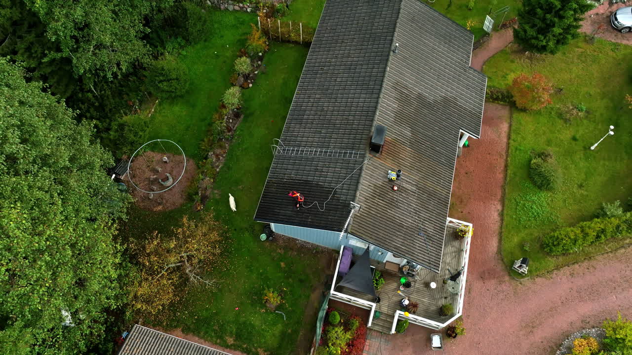 Aerial tilt shot rising above a person washing a house roof, dog on yard, fall day