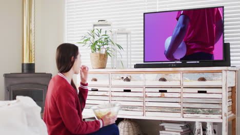 mujer caucásica viendo la televisión con un jugador de rugby afroamericano con la pelota en la pantalla