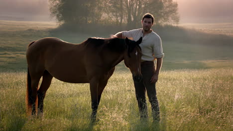 a man stands with a horse in a misty, golden field during sunrise or sunset