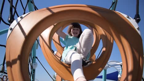 young girl climbing through playground rings smiling on sunny day